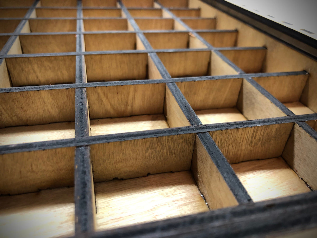 Close-up view of a laser-cut wooden typeset drawer with internal dividers. The drawer features a grid layout with individual cubby spaces. The internal dividers are 3/4" tall, perfect for standard typesets.